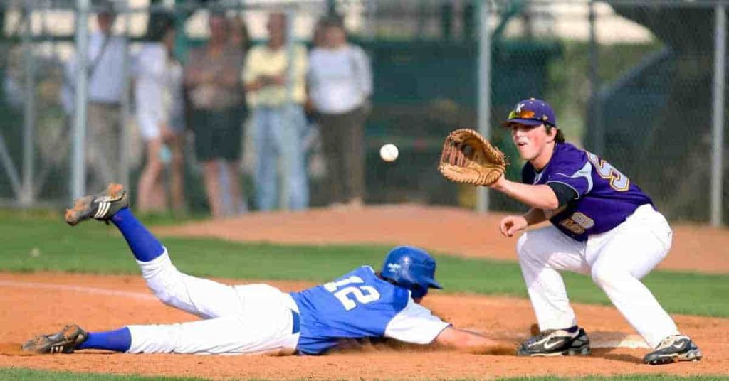 A player in a blue jersey dives to the ground attempting to catch a baseball, while a teammate in a purple jersey stands ready to field it — illustrating the dedication and effort behind roles like bullpen catcher, whose salary reflects their crucial behind-the-scenes contributions.